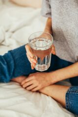 woman sat cross legged on bed holding a glass of water