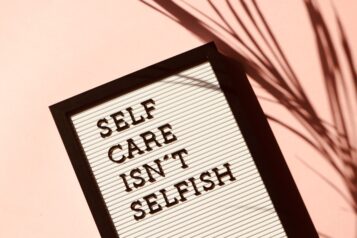 black and white letter board saying "self care isn't selfish" on a pink background with a leaf next to it